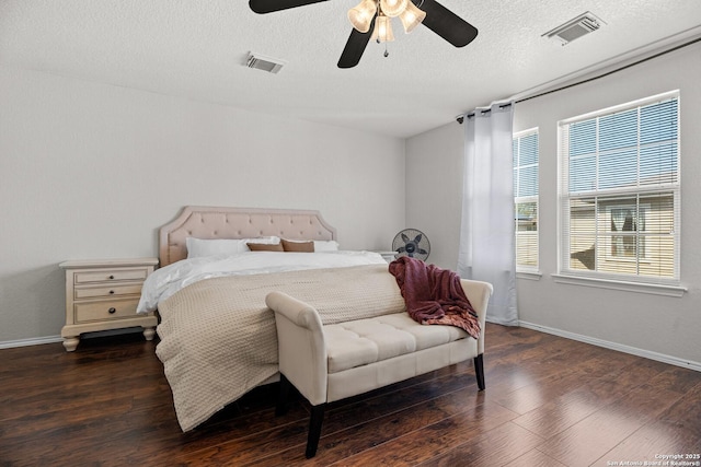 bedroom with ceiling fan, a textured ceiling, visible vents, and dark wood-style flooring