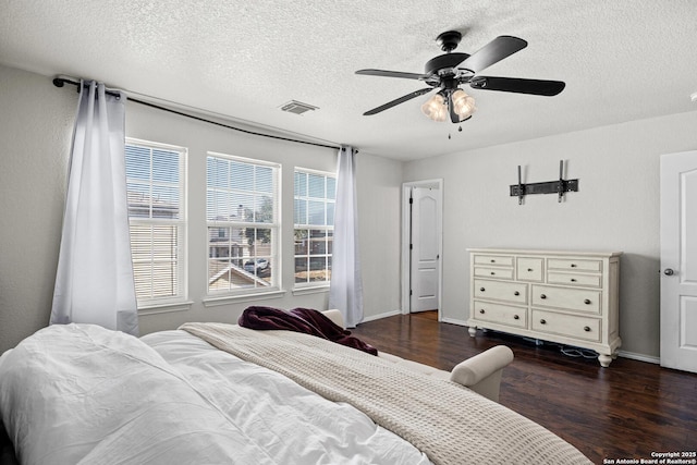 bedroom featuring ceiling fan, a textured ceiling, dark wood-style flooring, visible vents, and baseboards