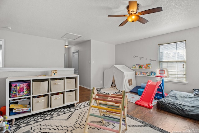 rec room with a textured ceiling, ceiling fan, wood finished floors, and attic access