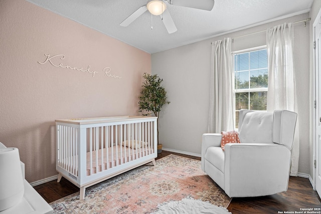 bedroom with a crib, a ceiling fan, baseboards, and wood finished floors