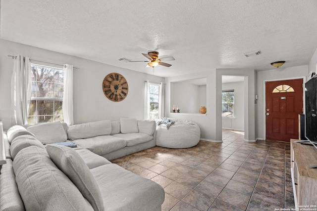 living area featuring a ceiling fan, a healthy amount of sunlight, visible vents, and a textured ceiling