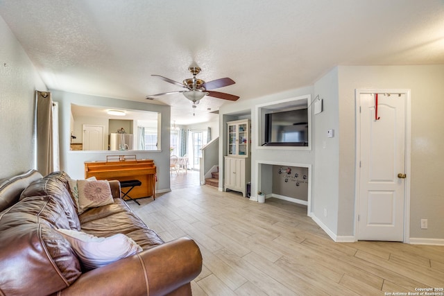 living room with light wood-type flooring, ceiling fan, stairway, and a textured ceiling