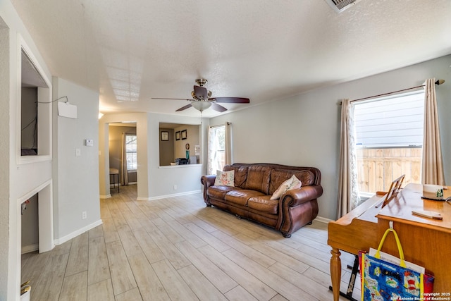 living area with a textured ceiling, light wood-style flooring, a ceiling fan, visible vents, and baseboards