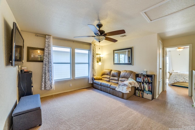 carpeted living room with a textured ceiling, ceiling fan, visible vents, baseboards, and attic access