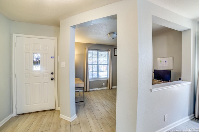 entrance foyer with light wood finished floors, baseboards, and a textured ceiling