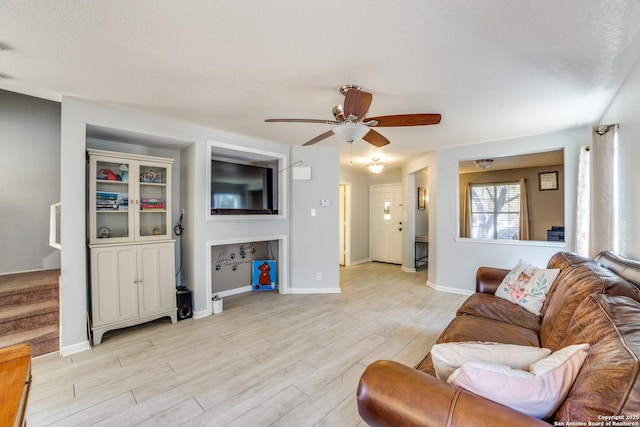 living area with stairs, light wood finished floors, a ceiling fan, and baseboards