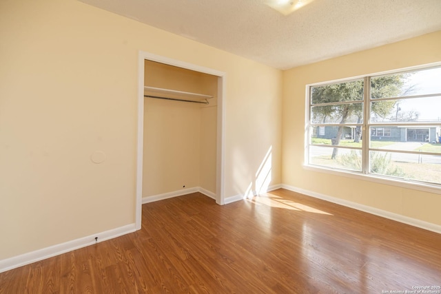 unfurnished bedroom with a closet, a textured ceiling, baseboards, and wood finished floors