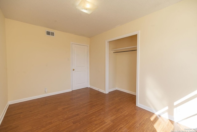 unfurnished bedroom with a textured ceiling, wood finished floors, visible vents, and baseboards