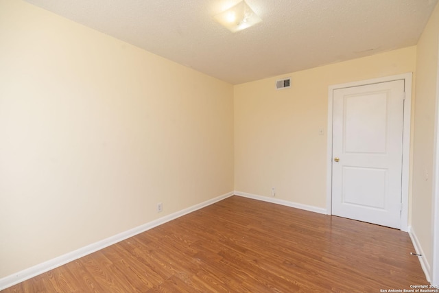 spare room featuring a textured ceiling, wood finished floors, visible vents, and baseboards