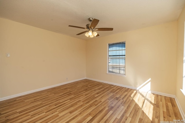 empty room featuring a textured ceiling, a ceiling fan, light wood-style flooring, and baseboards