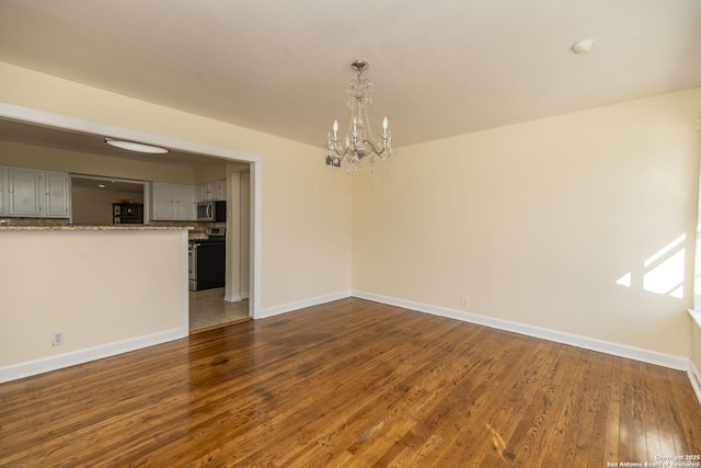 spare room featuring a chandelier, hardwood / wood-style flooring, and baseboards