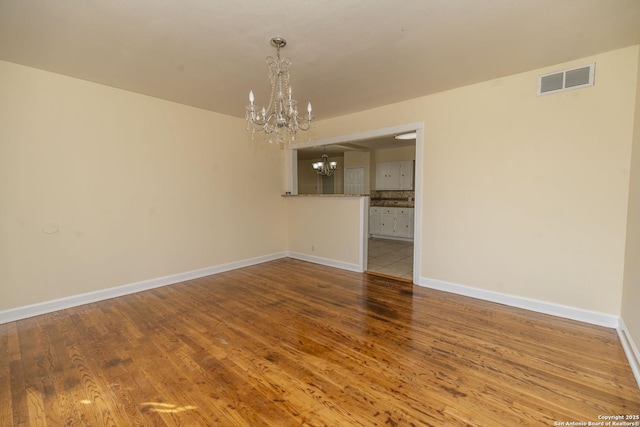 unfurnished room with baseboards, wood finished floors, visible vents, and a notable chandelier