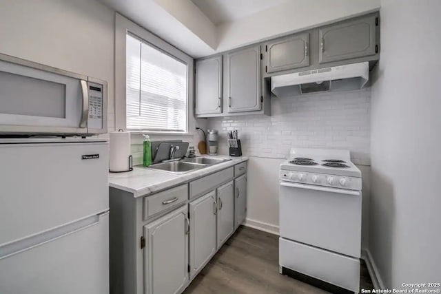 kitchen with gray cabinetry, under cabinet range hood, white appliances, light countertops, and tasteful backsplash