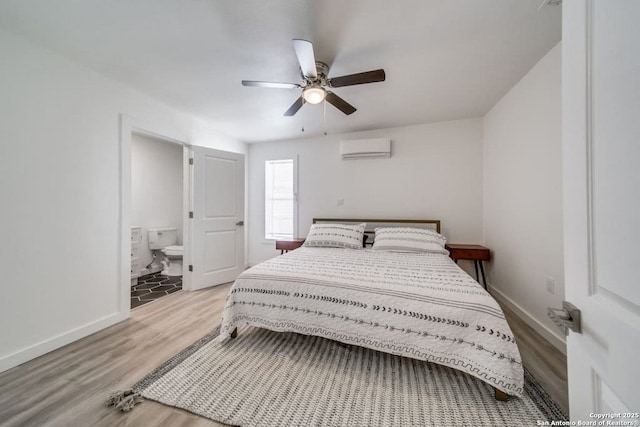 bedroom featuring baseboards, connected bathroom, a ceiling fan, a wall unit AC, and light wood-type flooring