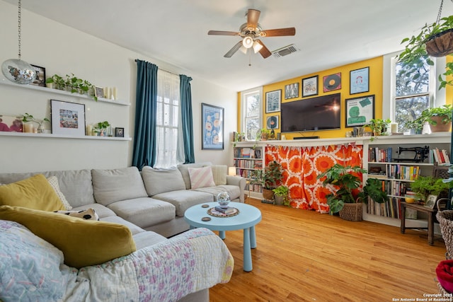 living room featuring ceiling fan, a fireplace, visible vents, and wood finished floors