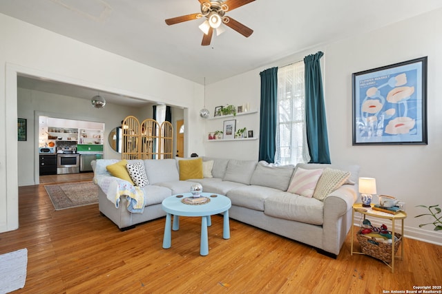 living room with ceiling fan, baseboards, and wood finished floors