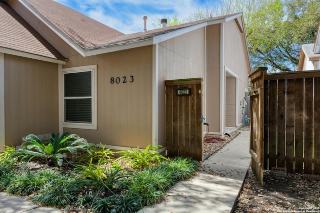 doorway to property featuring a shingled roof and fence