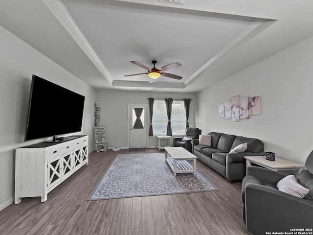 living area with baseboards, ceiling fan, wood finished floors, a tray ceiling, and crown molding