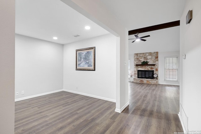 unfurnished living room with visible vents, dark wood-style floors, ceiling fan, a stone fireplace, and beam ceiling