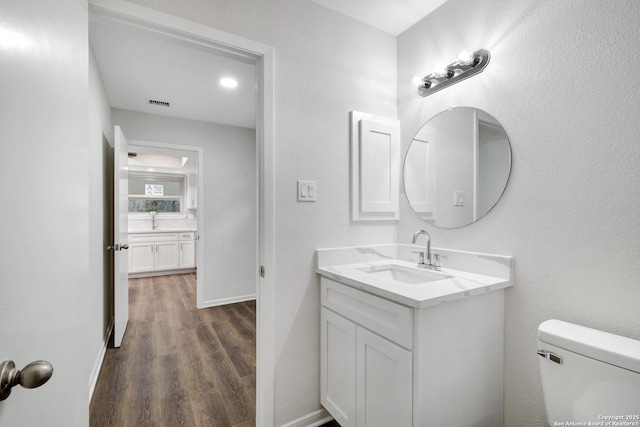 half bath with visible vents, vanity, toilet, and wood finished floors