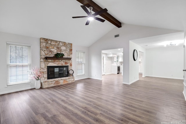 unfurnished living room with a healthy amount of sunlight, a fireplace, beamed ceiling, and wood finished floors