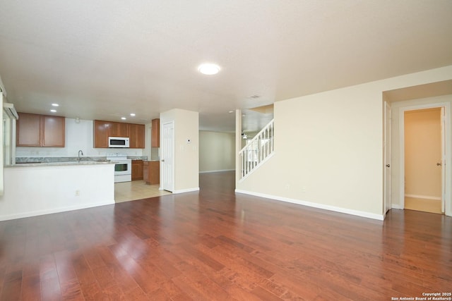 unfurnished living room with a sink, stairway, baseboards, and wood finished floors