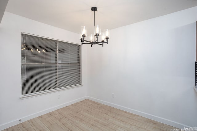 empty room with light wood finished floors, baseboards, and a chandelier