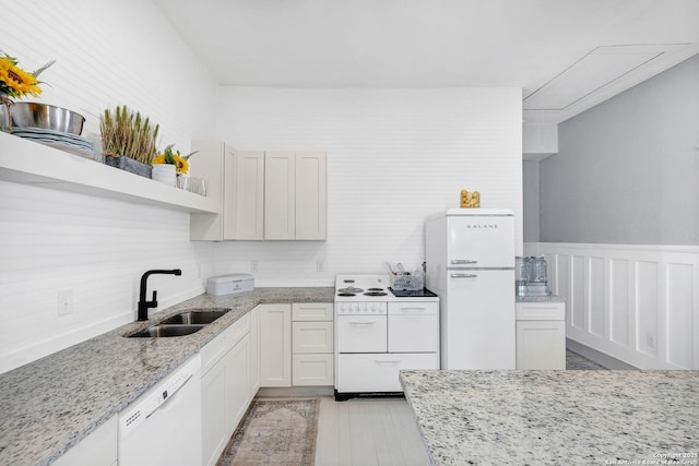 kitchen featuring white appliances, a sink, wainscoting, light stone countertops, and open shelves