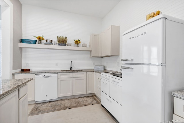 kitchen featuring white appliances, light wood finished floors, light stone counters, open shelves, and a sink