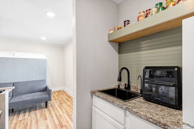 kitchen with light wood finished floors, baseboards, light stone countertops, white cabinetry, and a sink