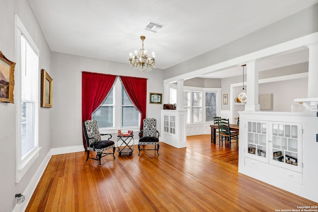 sitting room with visible vents, hardwood / wood-style flooring, decorative columns, and a notable chandelier