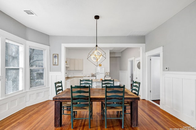 dining room featuring a decorative wall, wood finished floors, visible vents, wainscoting, and an inviting chandelier