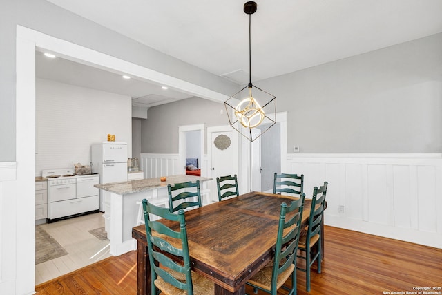 dining space with light wood finished floors, recessed lighting, a chandelier, and wainscoting