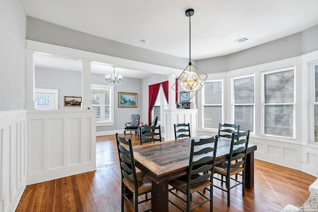 dining space with a notable chandelier, a decorative wall, visible vents, wainscoting, and wood-type flooring