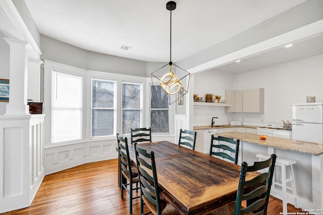 dining room with light wood finished floors, decorative columns, visible vents, and a decorative wall