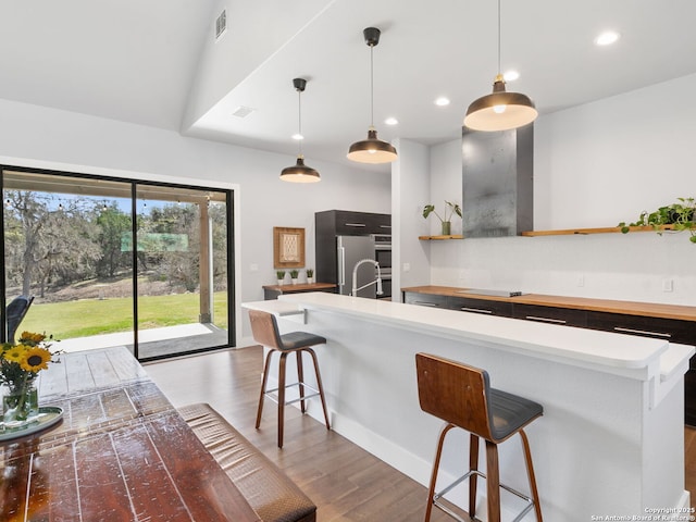 kitchen with pendant lighting, open shelves, a kitchen breakfast bar, wood finished floors, and high end refrigerator