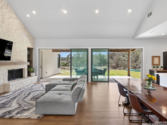 living area featuring high vaulted ceiling, visible vents, a stone fireplace, and wood finished floors