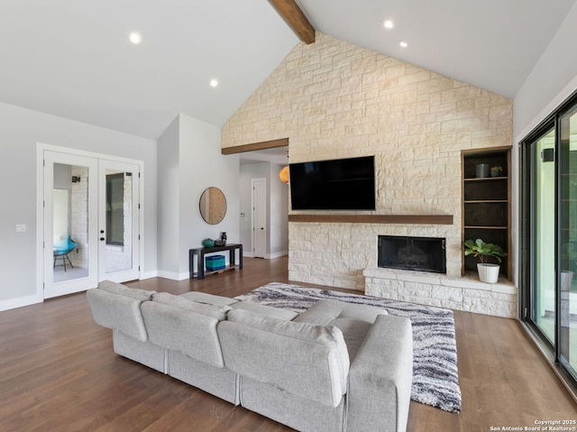 living room featuring beam ceiling, a stone fireplace, baseboards, and wood finished floors