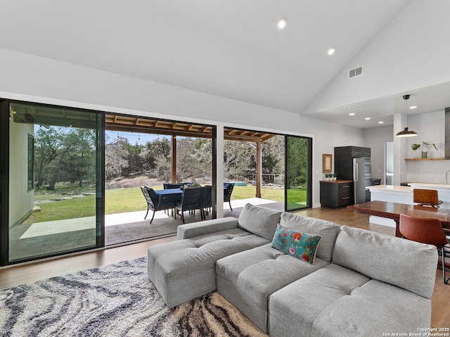 living room featuring light wood-type flooring, plenty of natural light, high vaulted ceiling, and recessed lighting