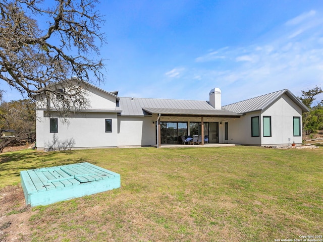 rear view of house featuring a yard, a patio area, metal roof, and a chimney