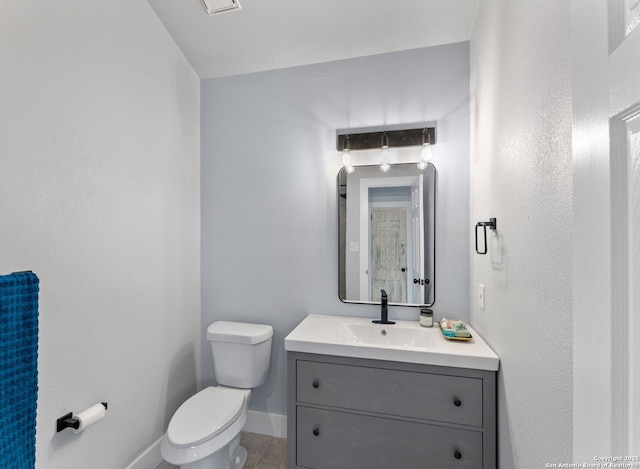 half bathroom with baseboards, vanity, and toilet