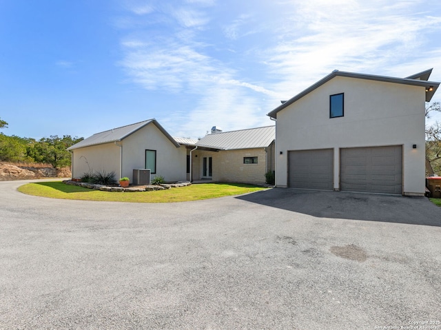 view of front of home featuring metal roof, aphalt driveway, cooling unit, a garage, and a front yard