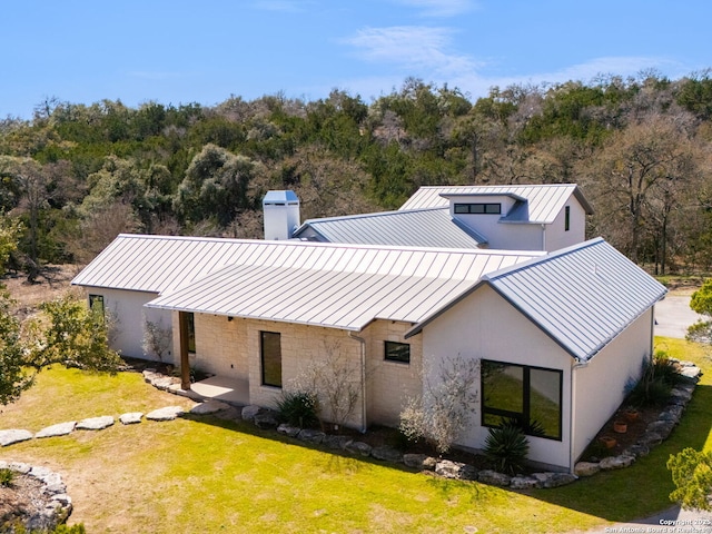 rear view of house with a chimney, metal roof, a standing seam roof, a yard, and a wooded view