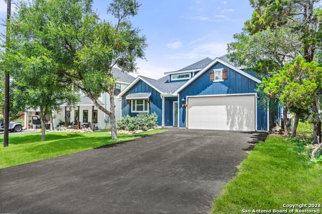 view of front of property featuring aphalt driveway, a garage, board and batten siding, and a front lawn