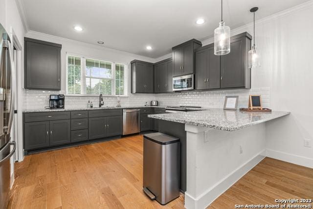 kitchen featuring light wood-style flooring, appliances with stainless steel finishes, a peninsula, crown molding, and a sink