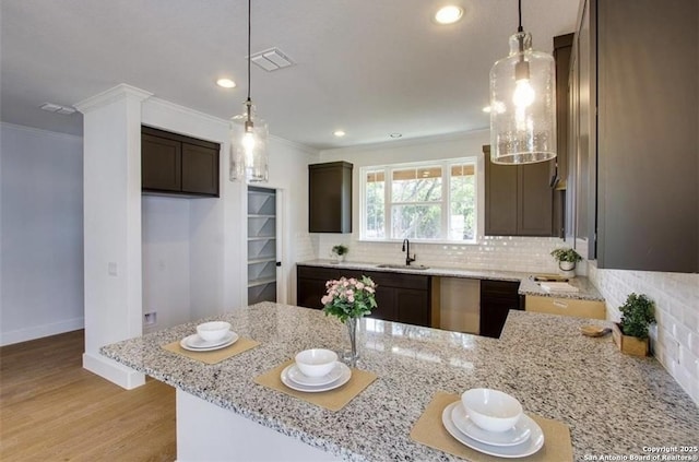 kitchen with dark brown cabinetry, a sink, light wood-style floors, ornamental molding, and light stone countertops