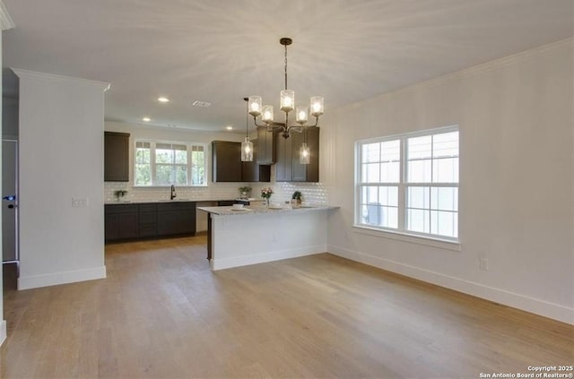 kitchen featuring tasteful backsplash, baseboards, crown molding, light wood-style floors, and a sink