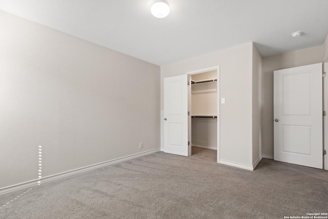 unfurnished bedroom featuring a closet, carpet, a walk in closet, and baseboards