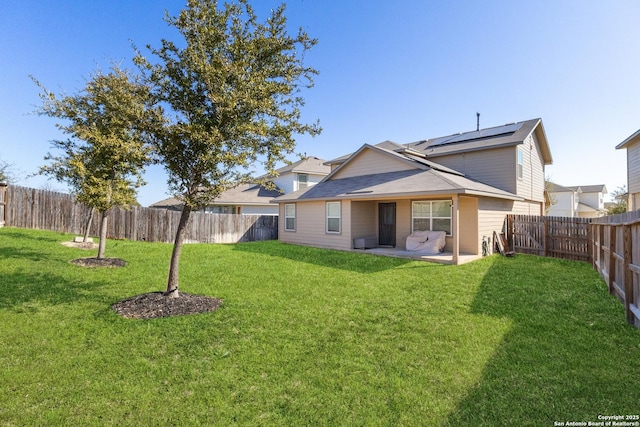 back of house featuring a patio area, a fenced backyard, a yard, and solar panels