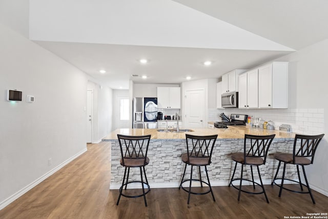 kitchen with stainless steel appliances, dark wood-type flooring, a peninsula, a sink, and white cabinetry